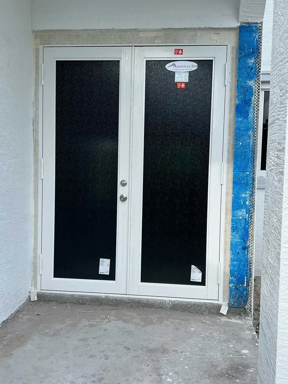 White double doors with privacy glass, newly installed in a concrete doorway.