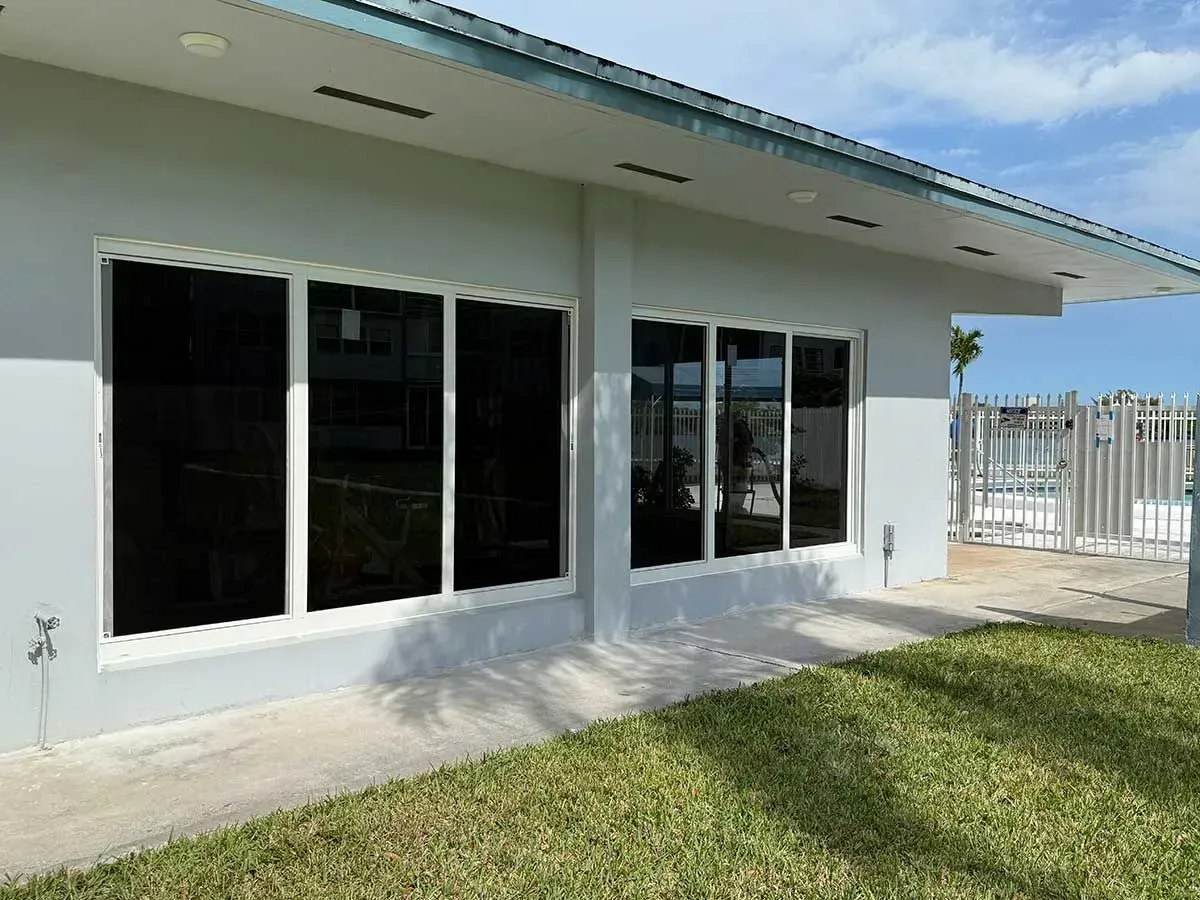 A light blue building with shaded windows, white frames, and a grassy area in front.