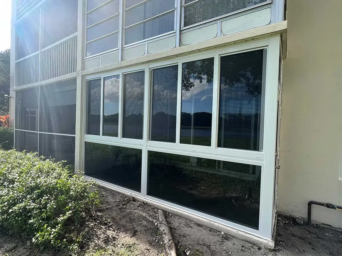 Exterior view of a building with white-framed windows and screen panels, reflecting sky and surrounding foliage.