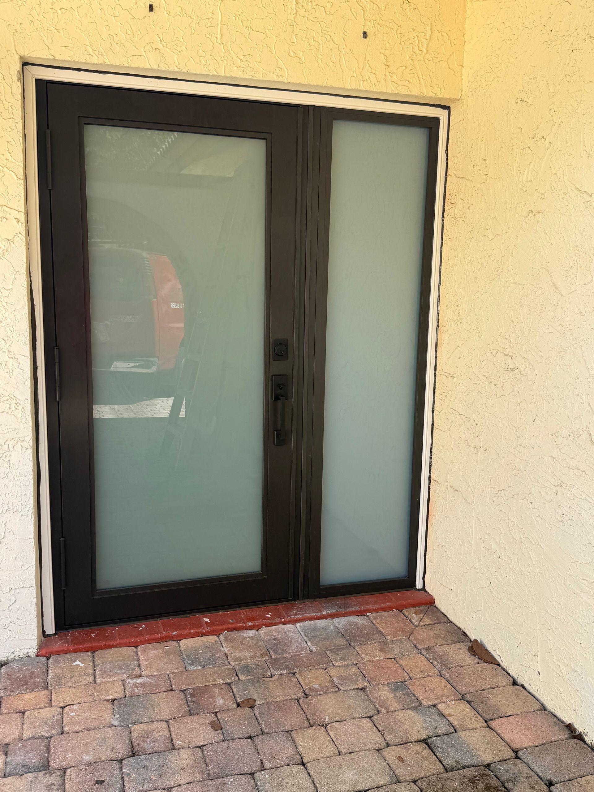 Dark double doors with frosted glass panels set in tan stucco, brick patio.