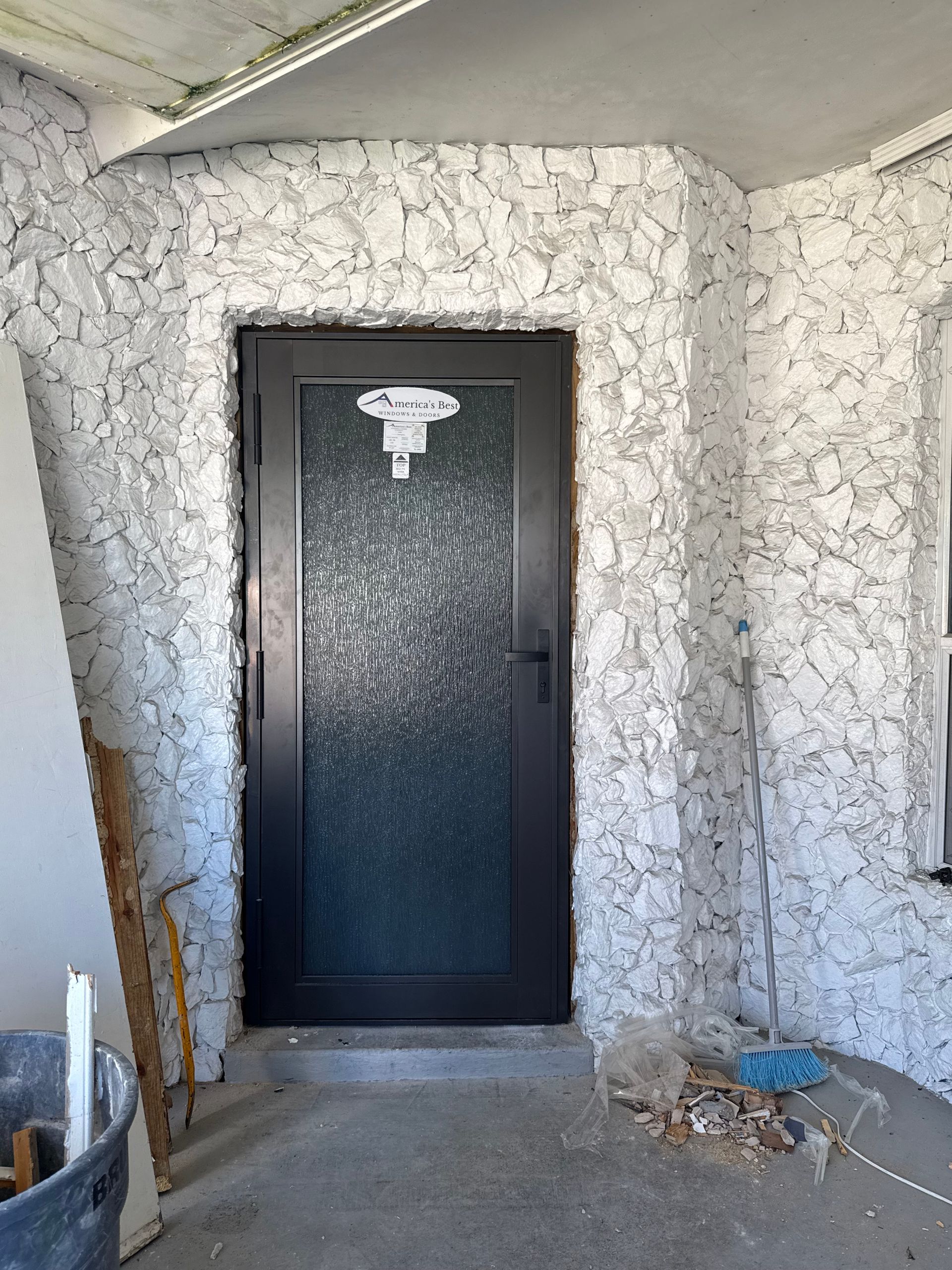 Dark door with frosted glass, set in a textured, white-painted wall; construction debris visible.