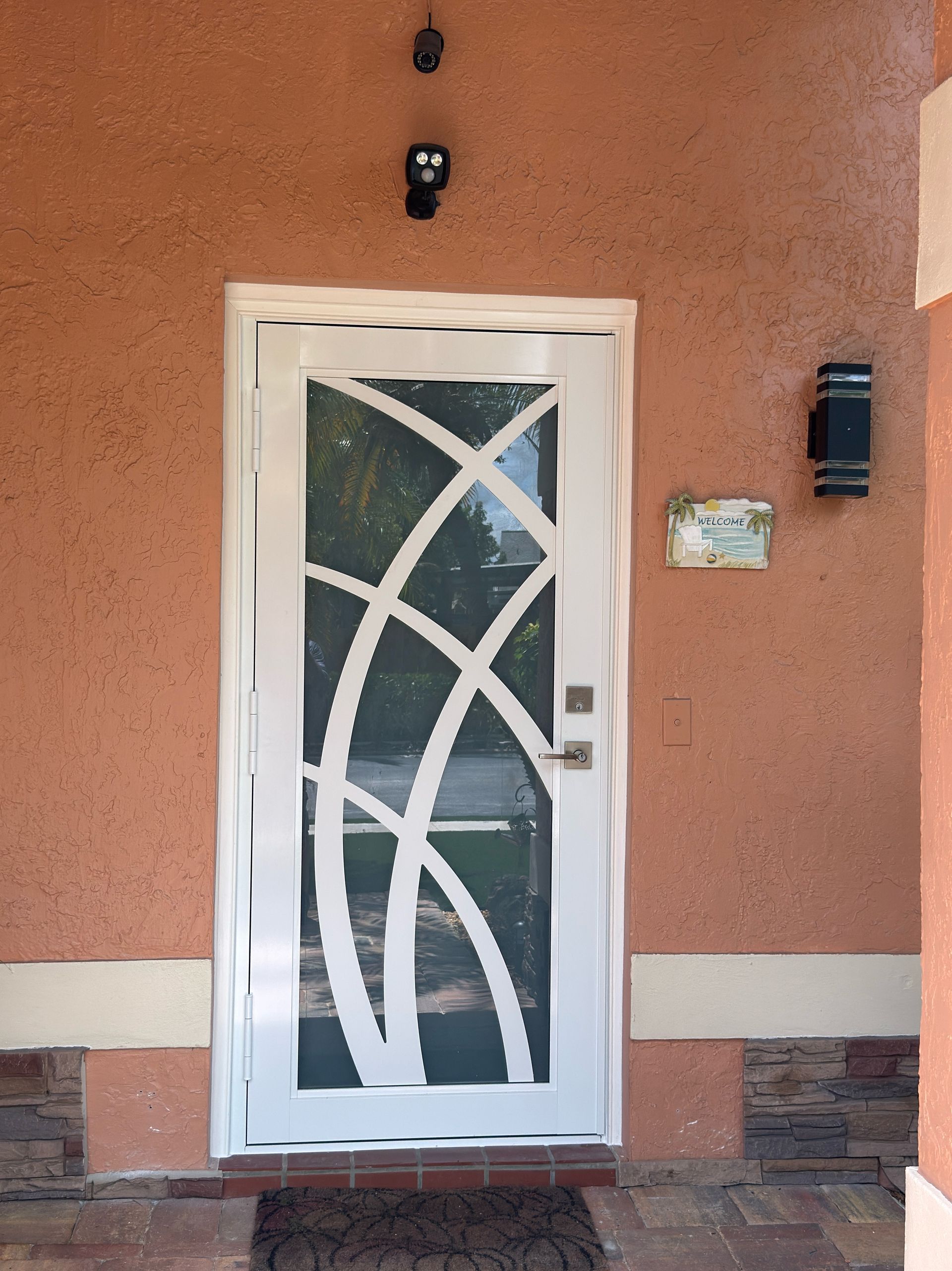 White front door with decorative glass on a peach stucco wall and brick trim.
