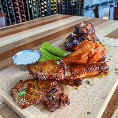 Platter of glazed grilled chicken wings with celery sticks and dipping sauce on a wooden board.