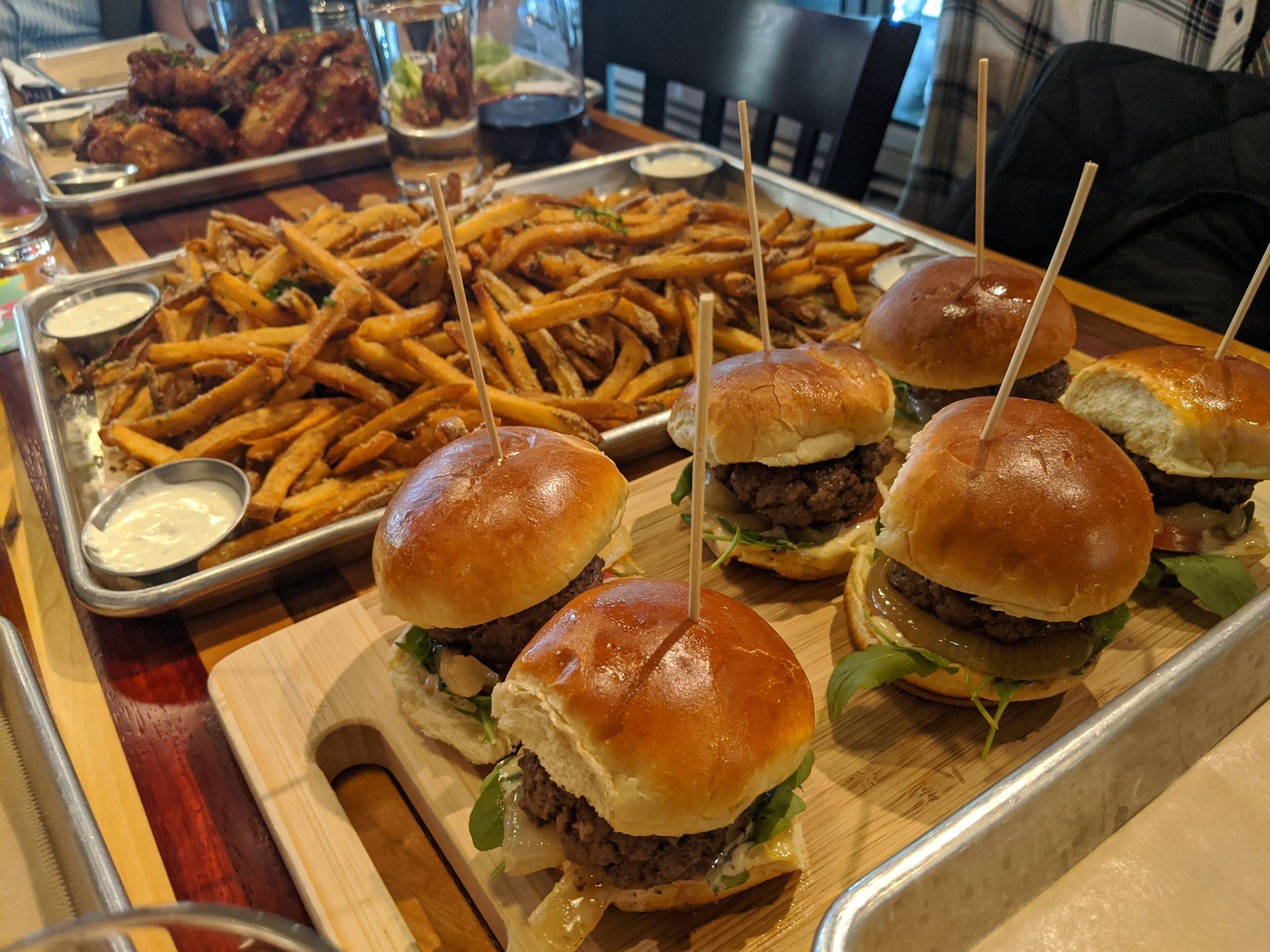 Tray of mini burgers and seasoned fries on a table, with dipping sauce and drinks in the background