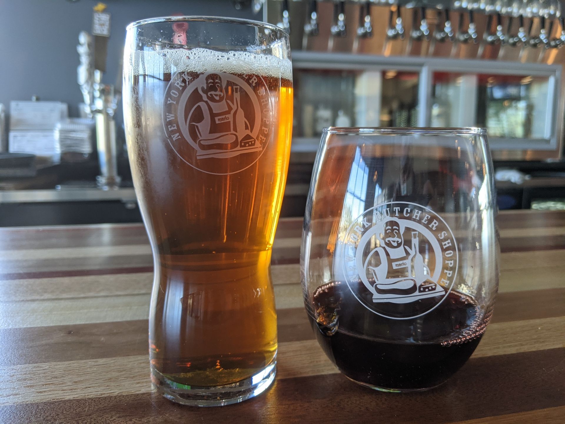 A pint of amber beer and a dark stout on a wooden bar in a brewery.