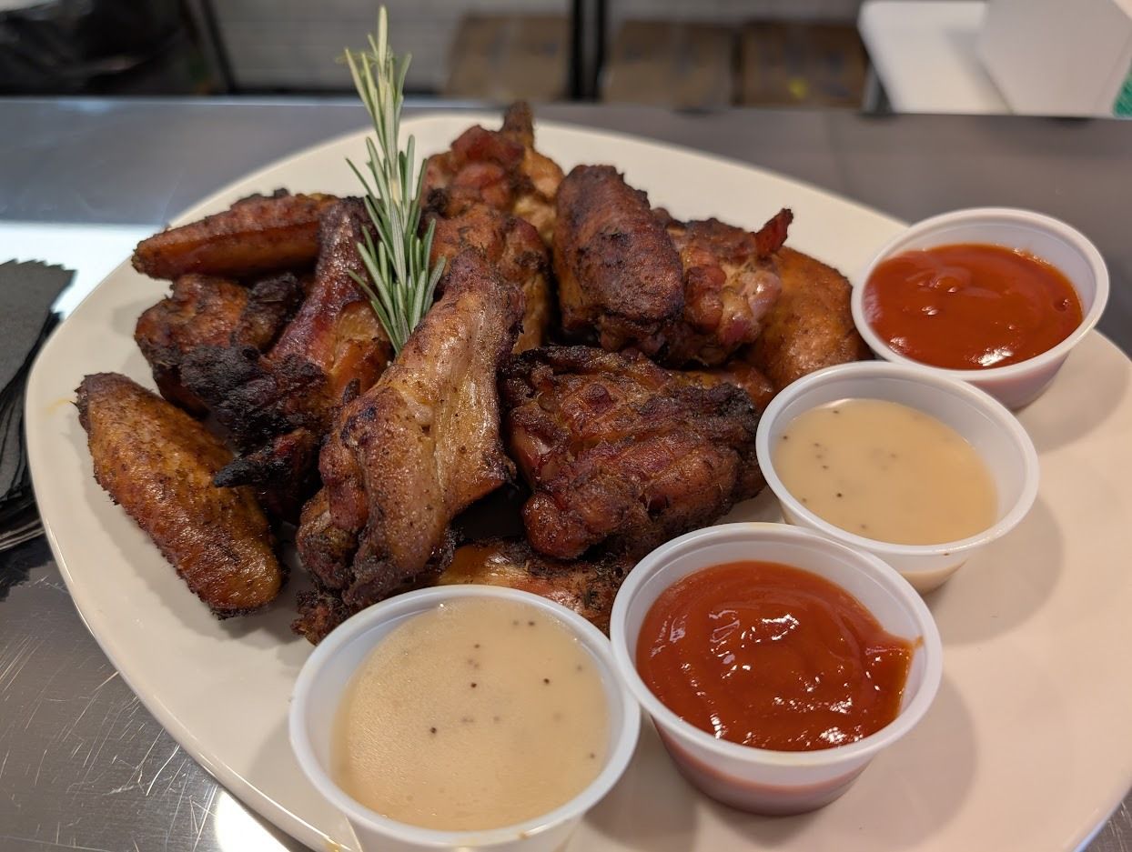 Plate of assorted fried chicken wings with rosemary and three dipping sauces on a table