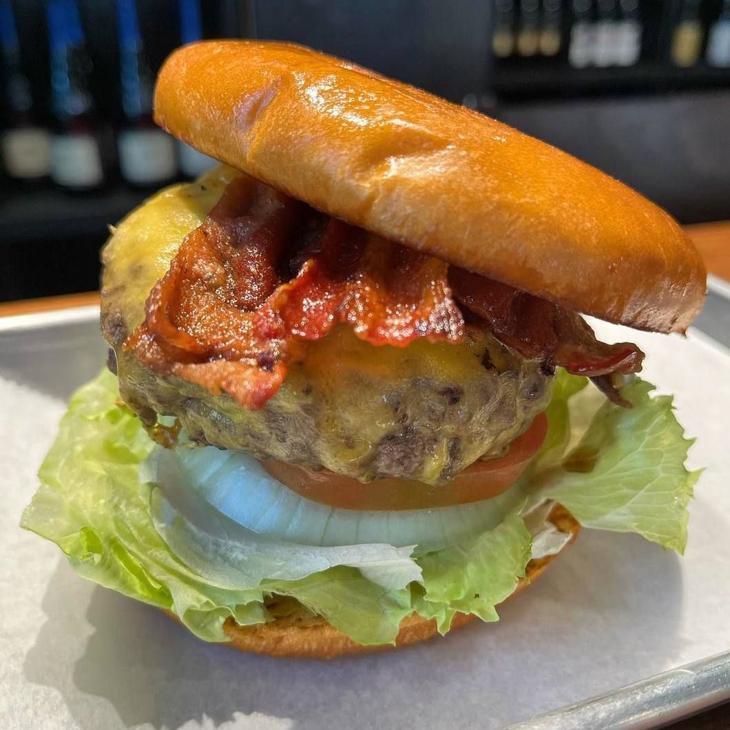 A bacon cheeseburger with lettuce and onion on a bun, served on a plate