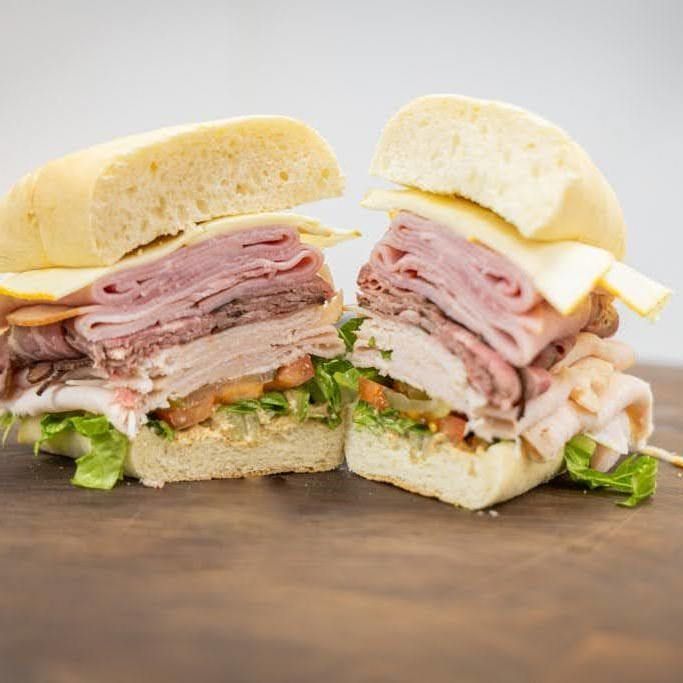 Cut sandwich with layers of ham, roast beef, cheese, greens, and a crusty roll on a wooden surface