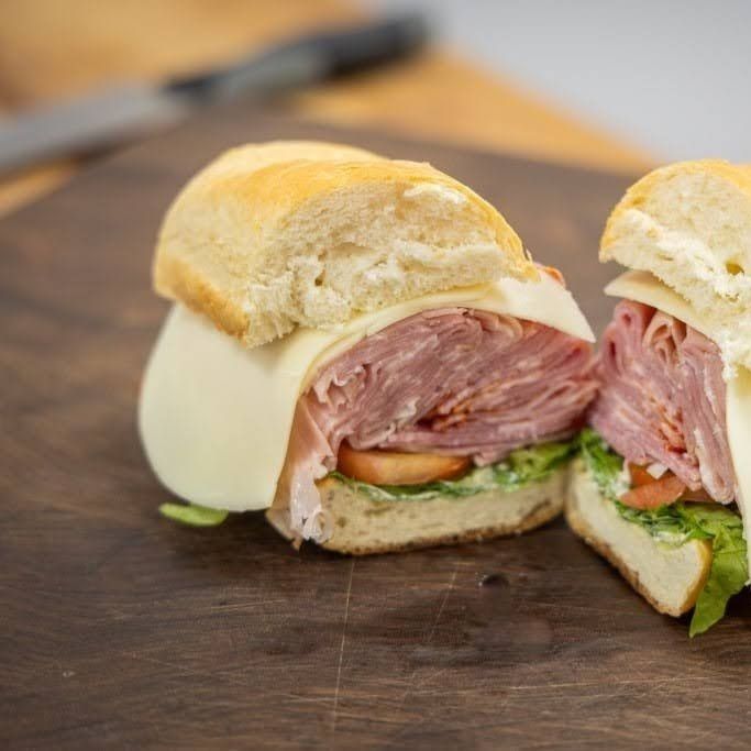 Close-up of a cut sandwich with ham, cheese, and greens on a wooden cutting board