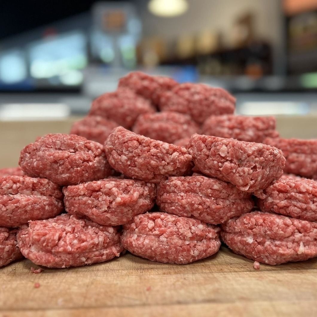 Stacked raw ground beef patties on a wooden cutting board in a kitchen