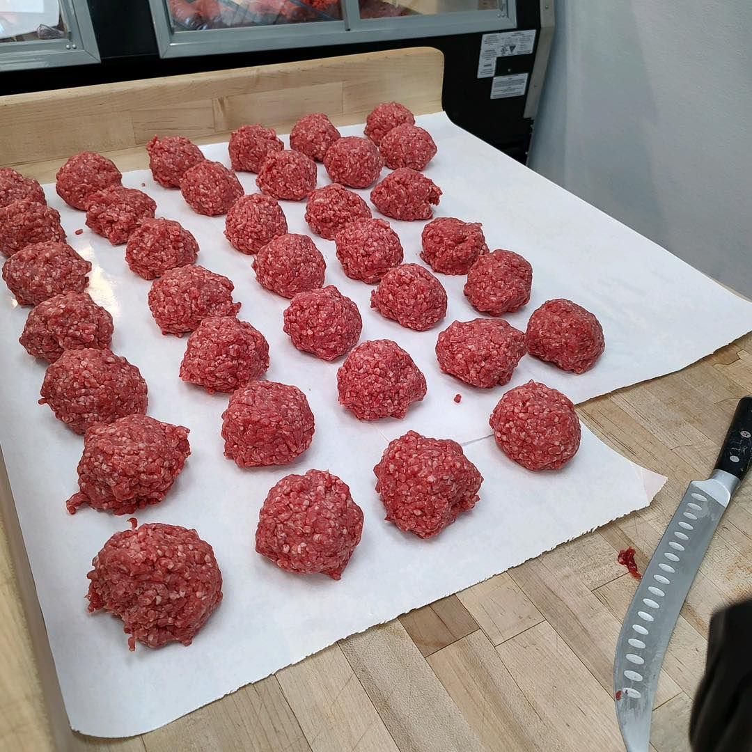 Raw red meat patties lined on parchment paper on a kitchen counter.