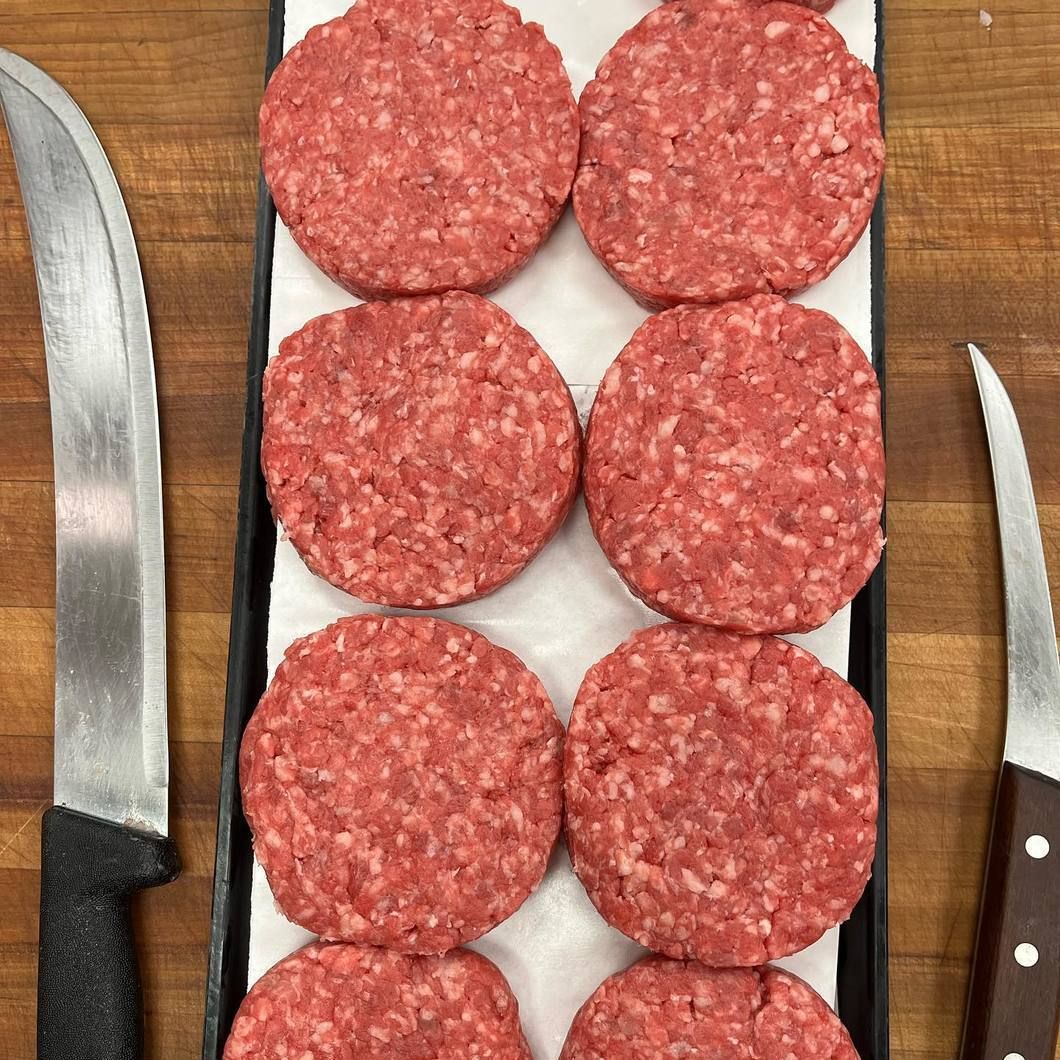 Raw hamburger patties on a cutting board with two knives on either side