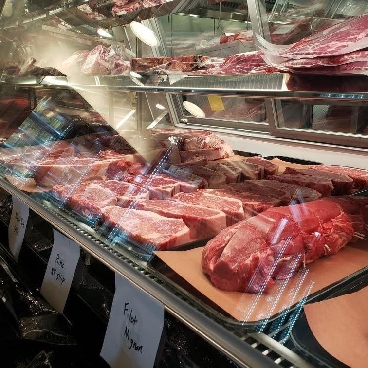 Butcher case with assorted raw steaks and cuts of meat displayed on trays behind glass.