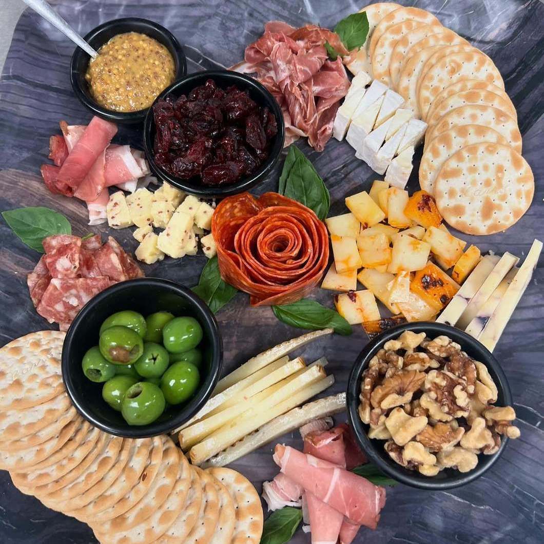 Charcuterie board with olives, cheeses, meats, crackers, nuts, and spreads on a dark slate platter