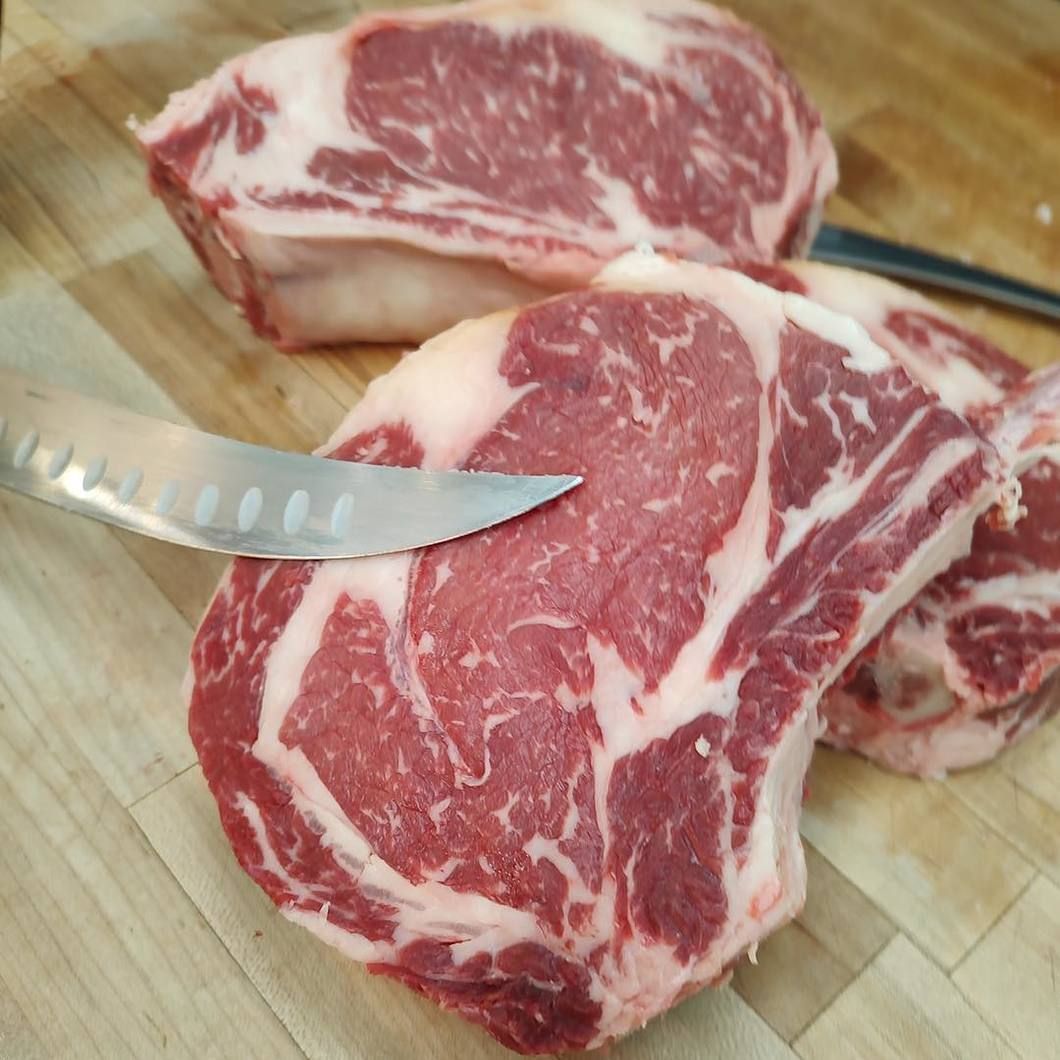 Raw marbled steak on a cutting board with a knife slicing into it