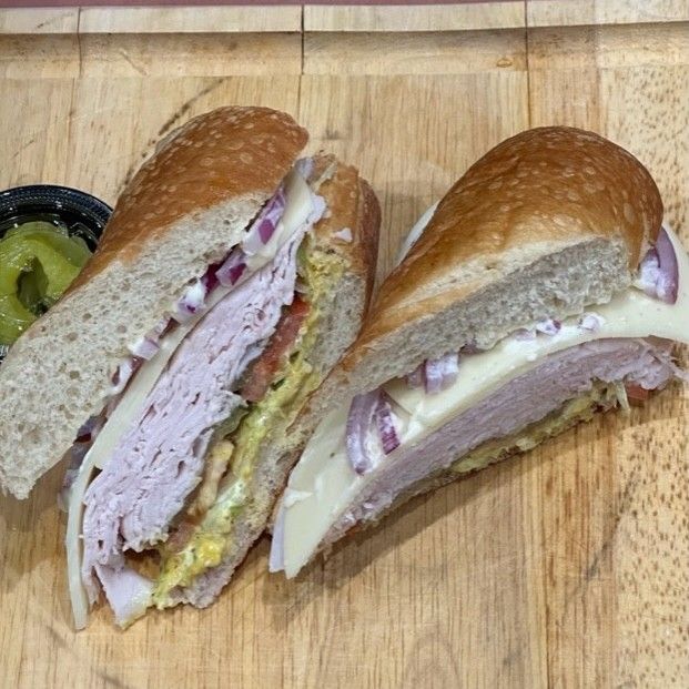 Two halved sandwiches with turkey, cheese, and onions on a wooden cutting board