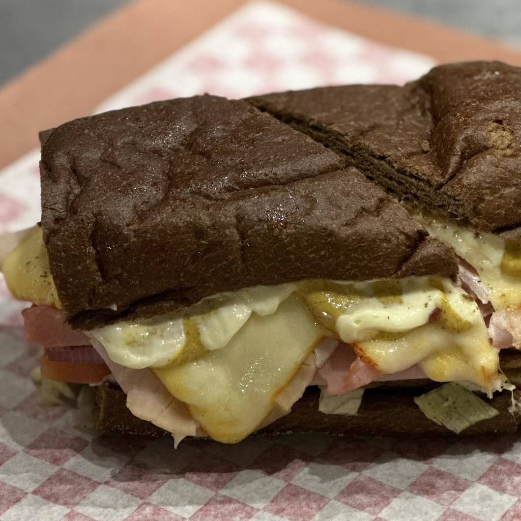 Close-up of a sandwich with dark bread, melted cheese, and deli meat on a plate