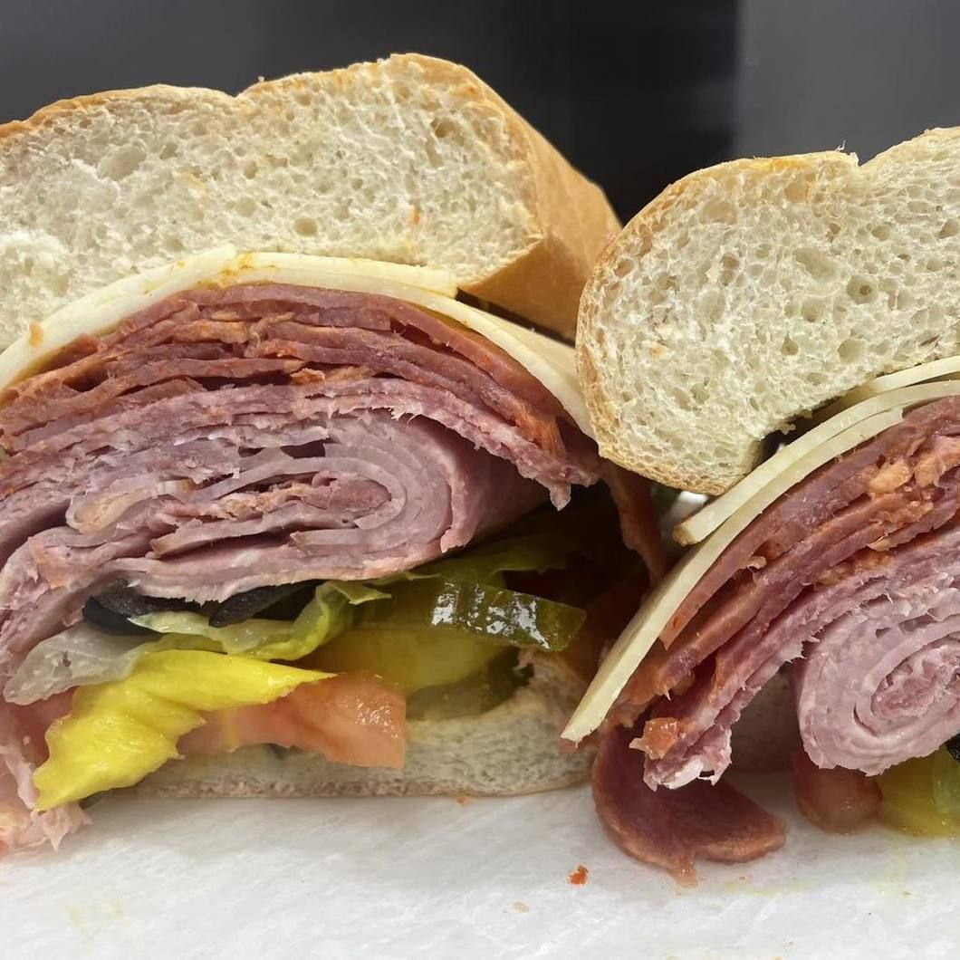 Close-up of two deli sandwiches with layered meat, cheese, and pickles on white bread.