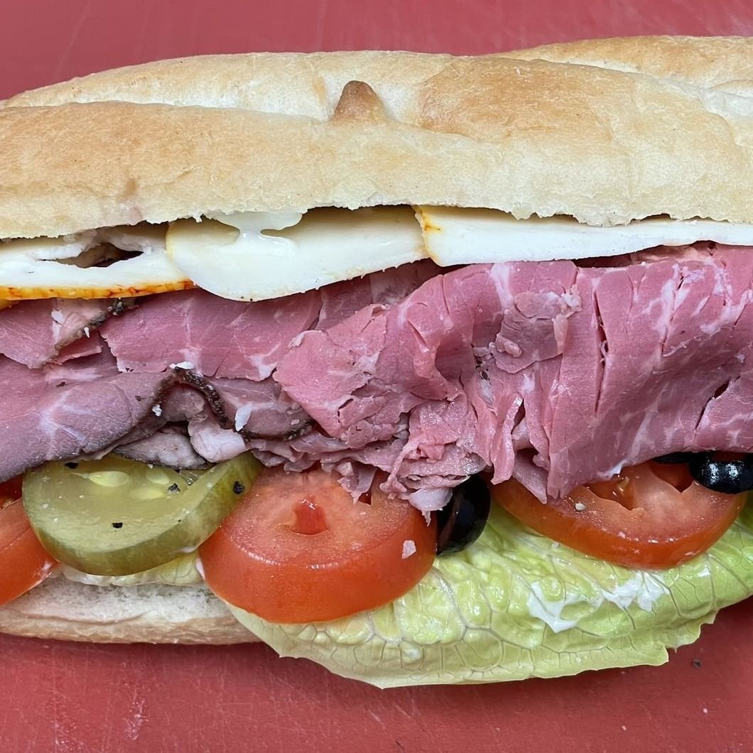 Roast beef sandwich with lettuce, tomato, pickles, and egg on a crusty roll