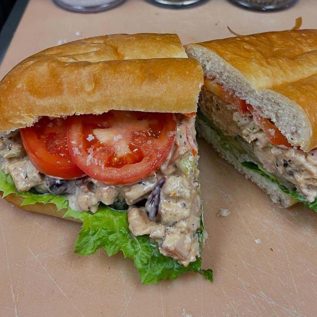 Two sandwich halves on a plate with tomato, lettuce, and creamy filling in a baguette roll