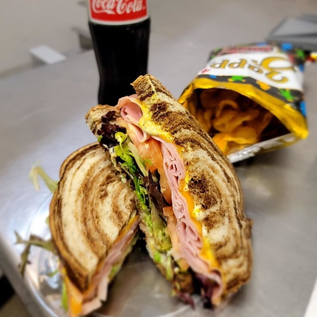 Sandwich cut in half with chips and a Coca-Cola bottle on a table.