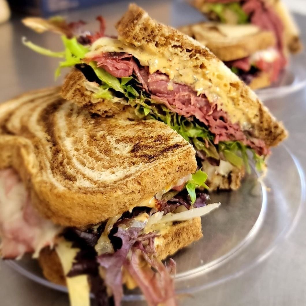 Grilled sandwich halves with layered meat and greens on a clear plate, close-up view