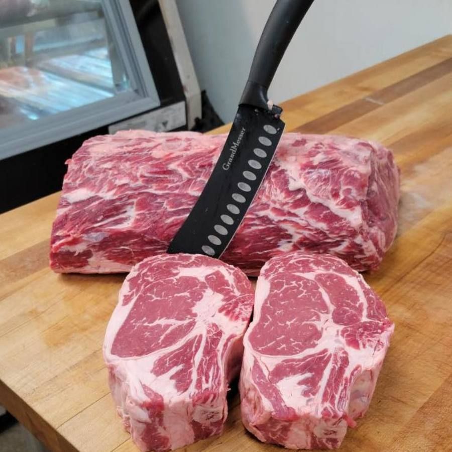 Raw marbled beef cuts on a wooden cutting board with a black knife handle visible