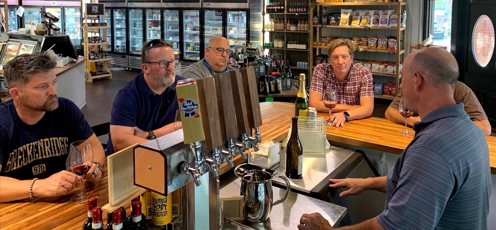 Five people chatting at a pub table with drinks in a casual bar setting