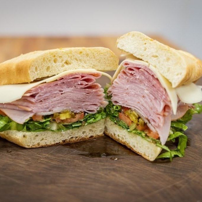 Ham and turkey sandwich with lettuce and mustard on a sliced baguette on a wooden board