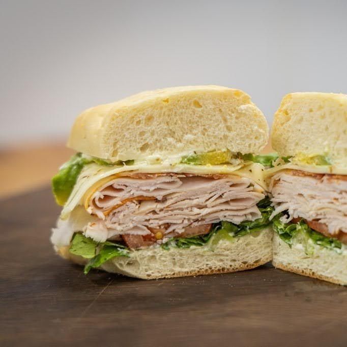 Turkey sandwich on a wooden board, sliced in half with lettuce and melted cheese visible
