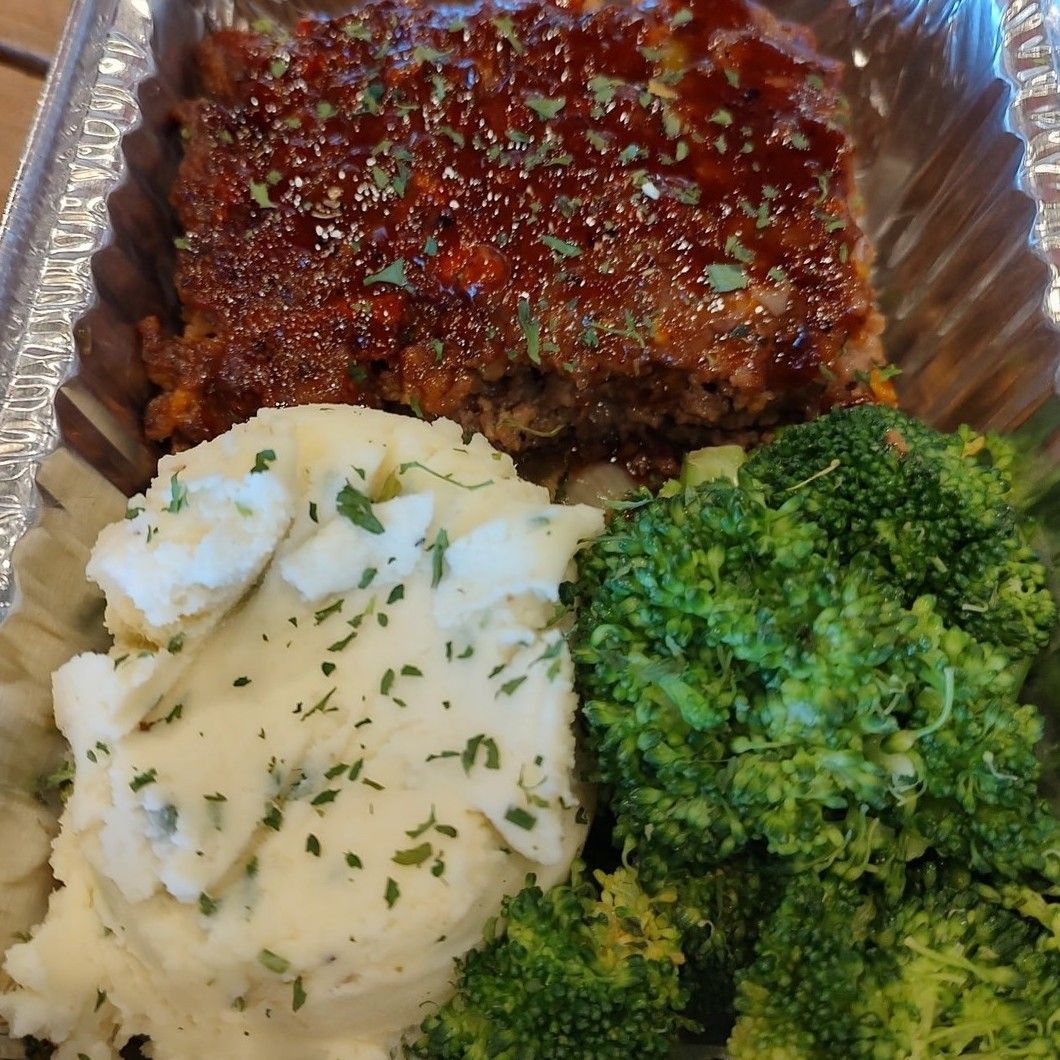 Takeout meal with meatloaf, mashed potatoes, and broccoli in a foil container