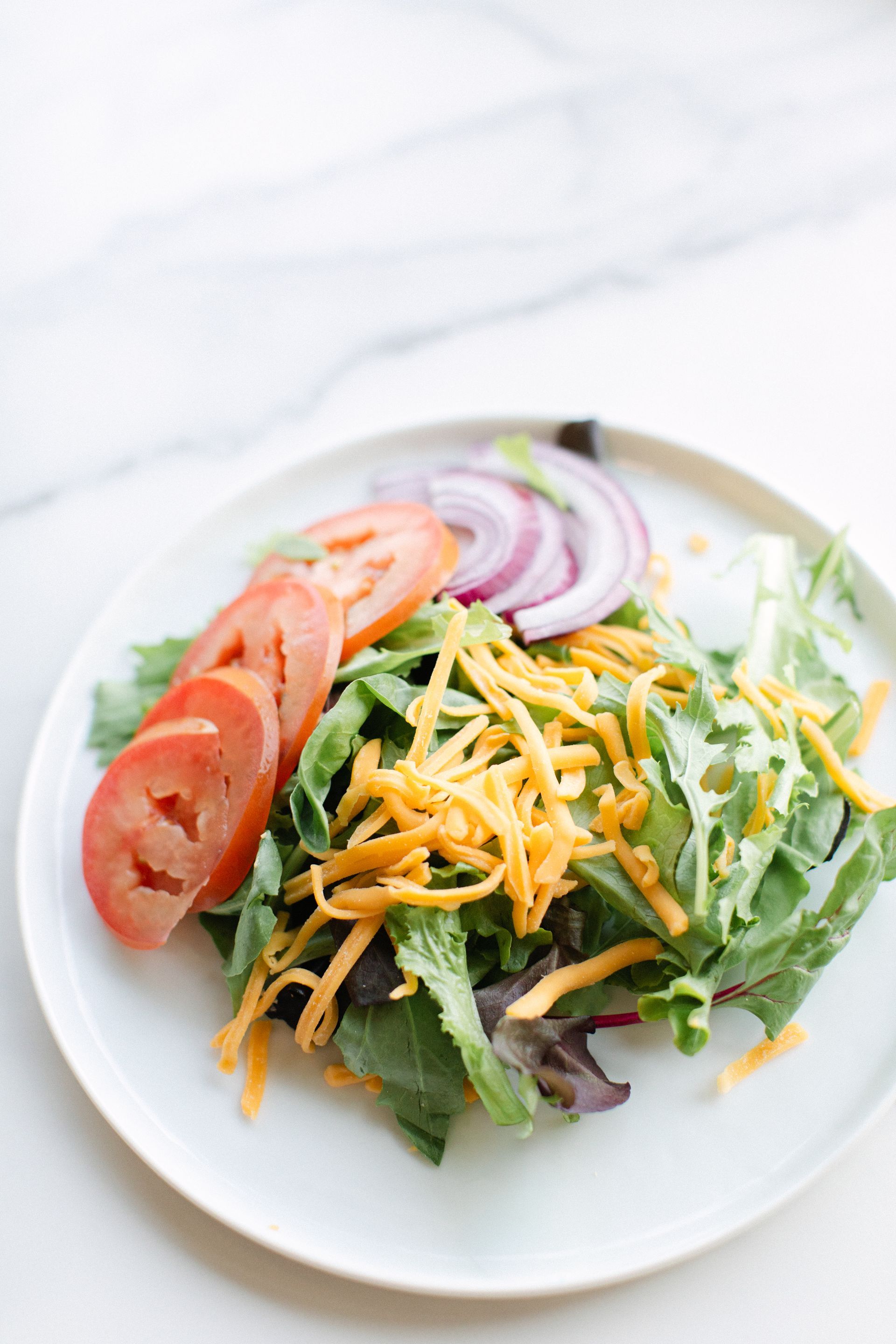 Salad with tomato, onion, cucumber, and shredded cheese on a white plate