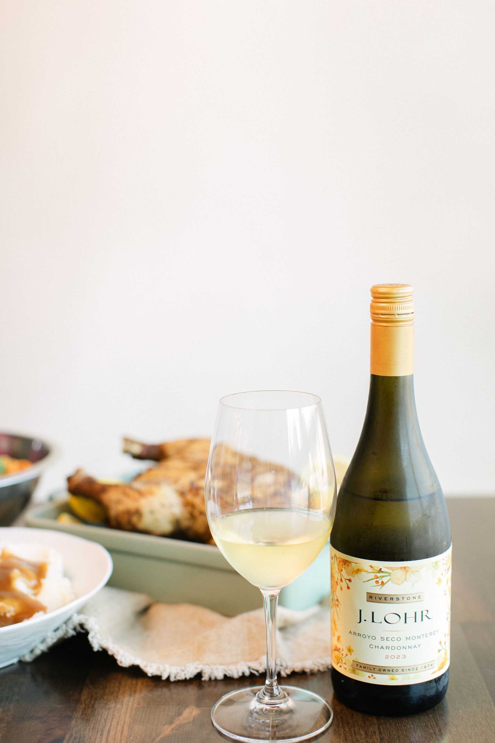 Wine bottle and empty glass on a table beside a platter of food.