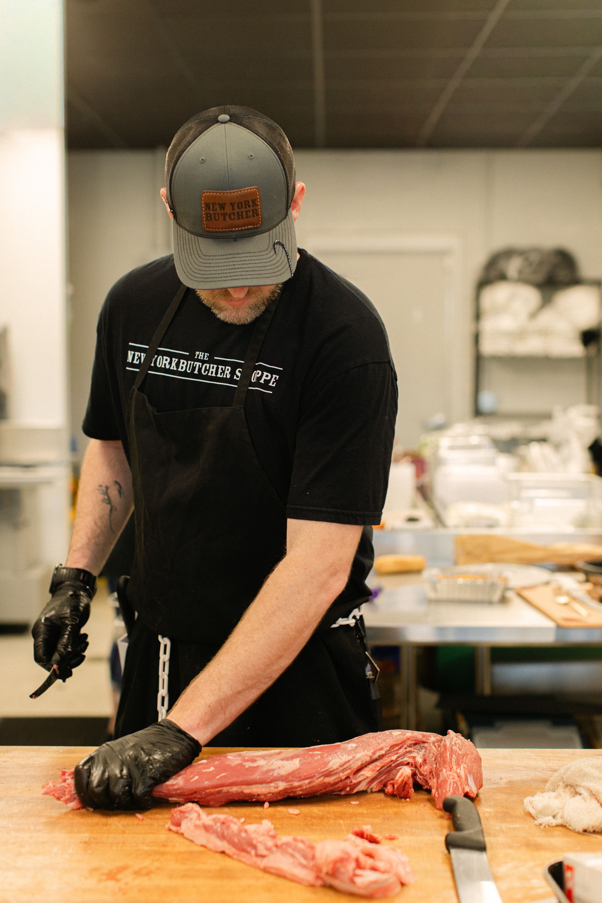Chef in black apron and gloves butchering a large fish on a cutting board in a kitchen.