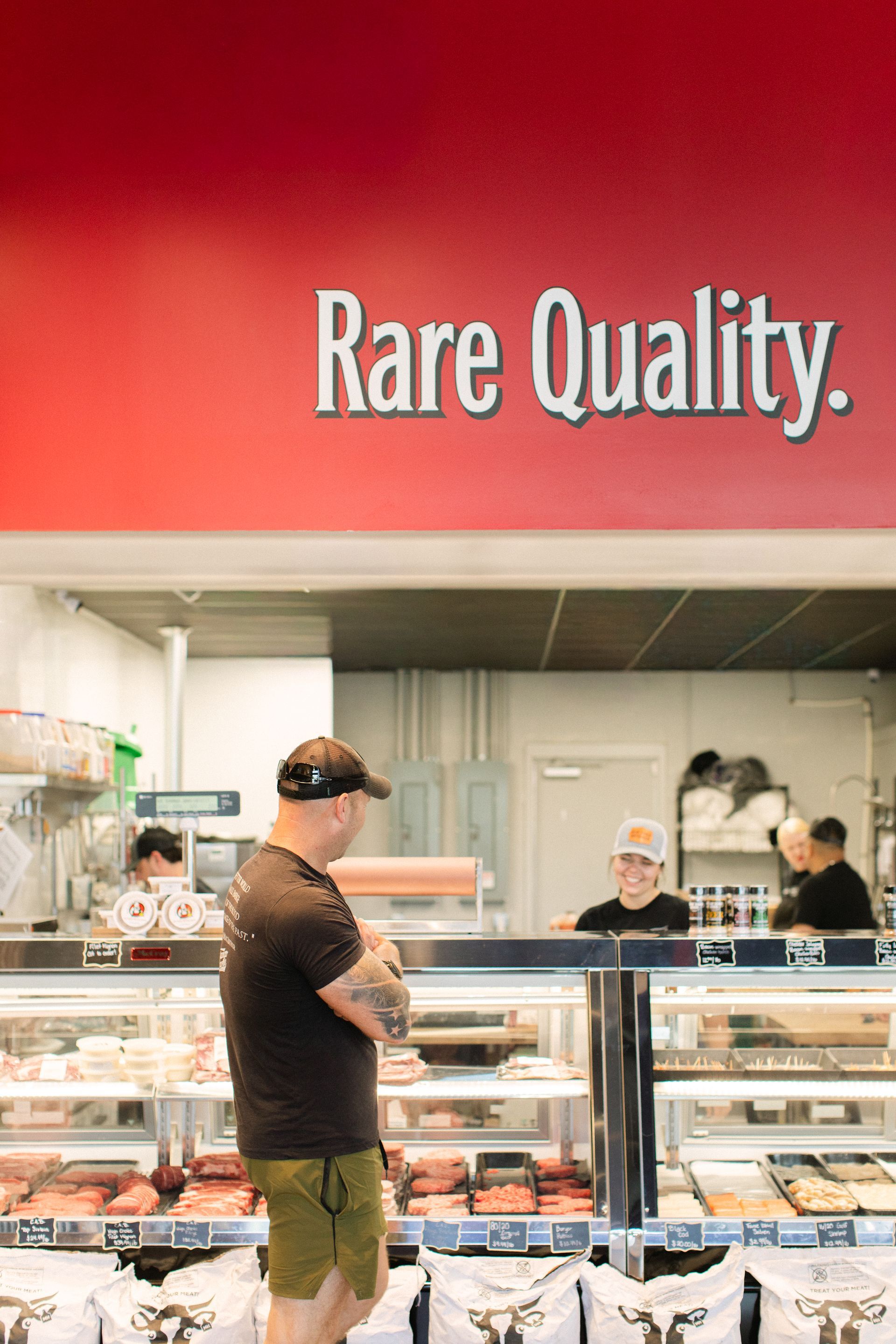 Bakery counter under a red “Rare Quality.” sign, with staff serving customers in a bright shop.