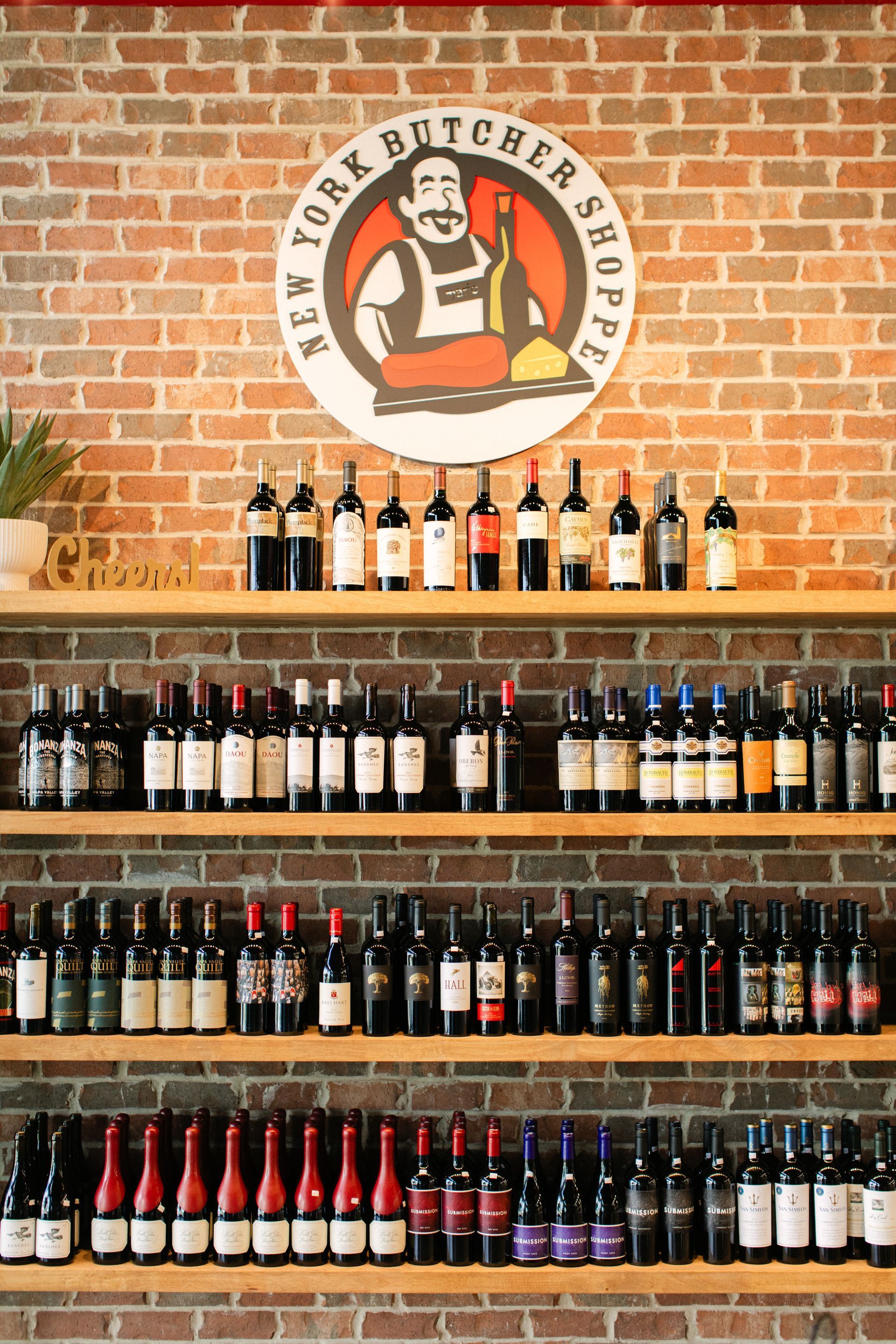 Wine bottles displayed on wooden shelves beneath a butcher shop sign on a brick wall