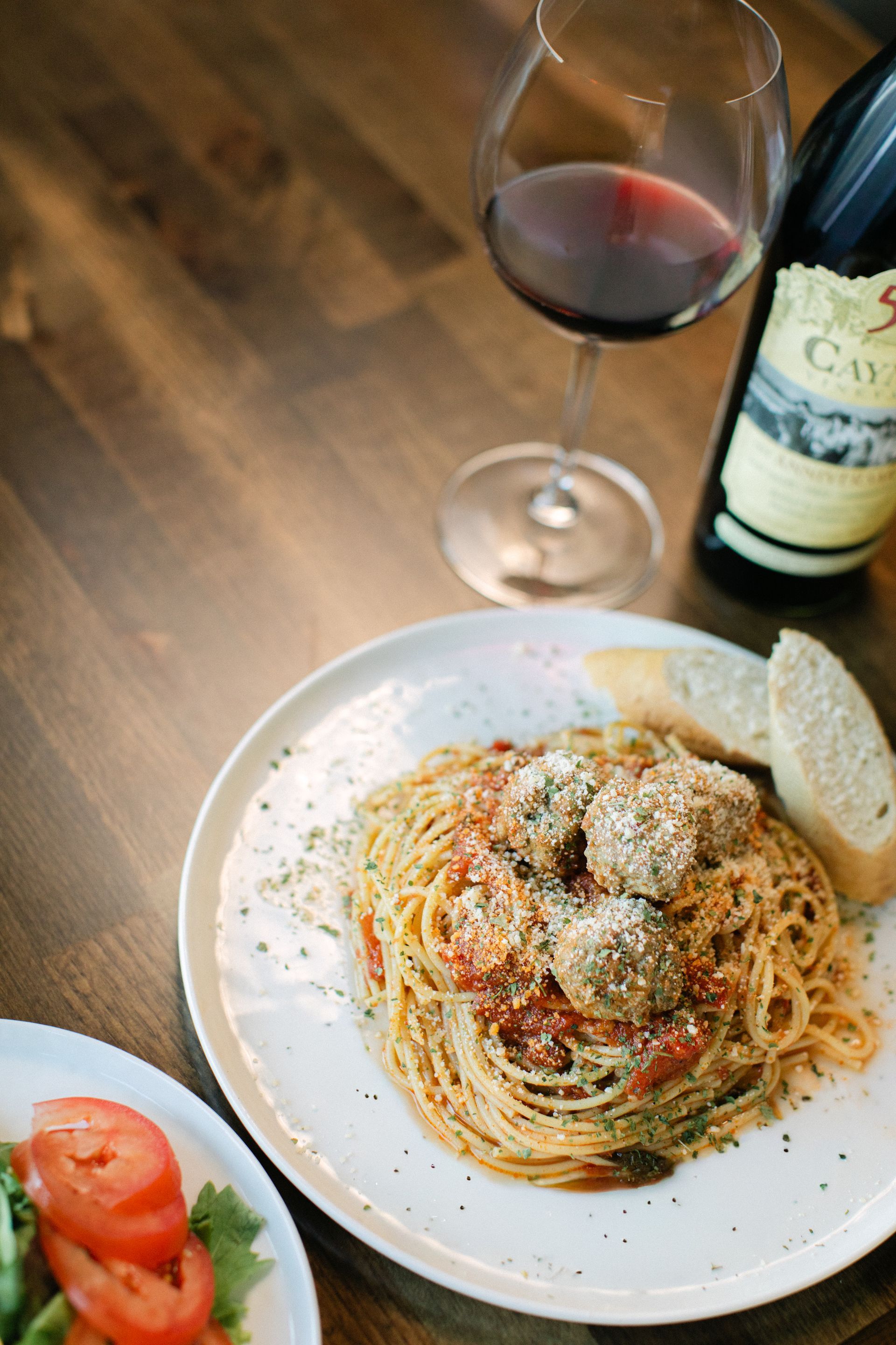 Plate of spaghetti with tomato sauce and cheese, salad, and a glass of red wine on a wooden table