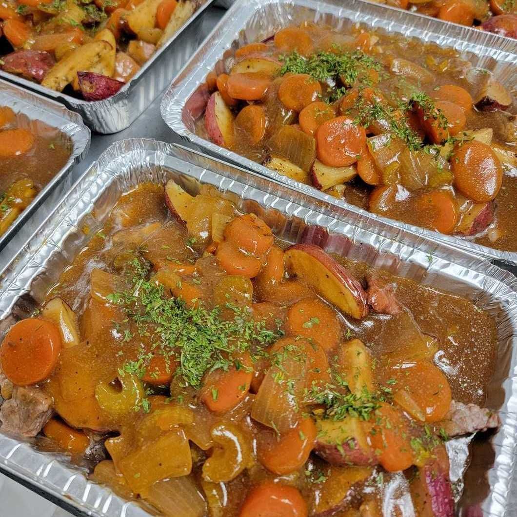 Foil trays of beef stew with carrots and herbs at a serving buffet