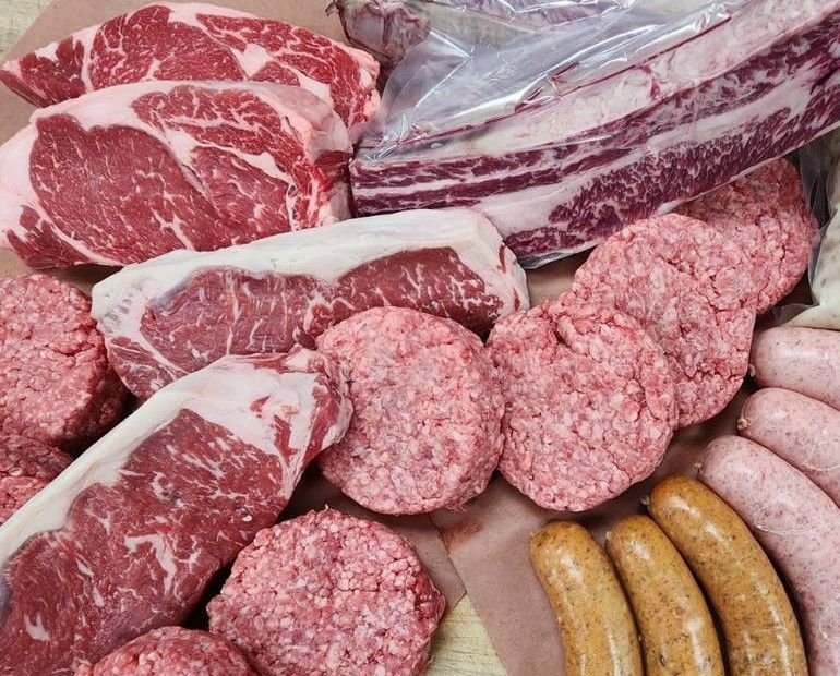 Assorted raw beef cuts and sausages arranged in a butcher display tray.