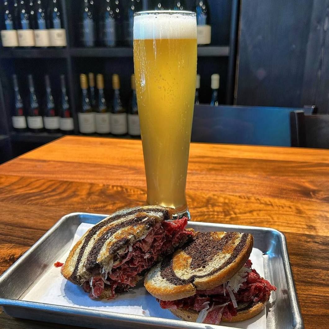 Beer and a sandwich on a metal tray on a wooden table in a bar.