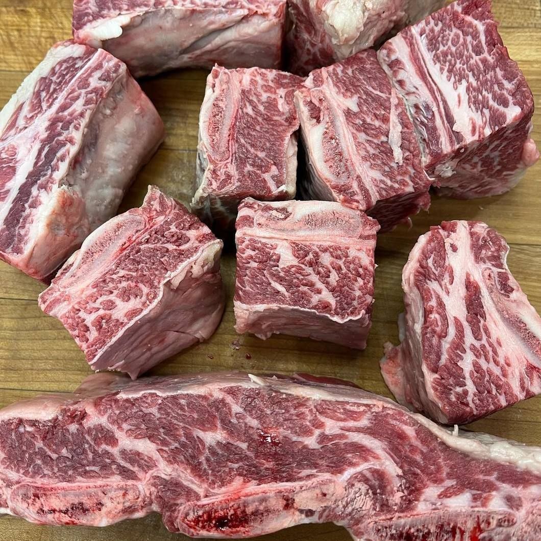Marbled raw beef short ribs cut into chunks on a wooden cutting board