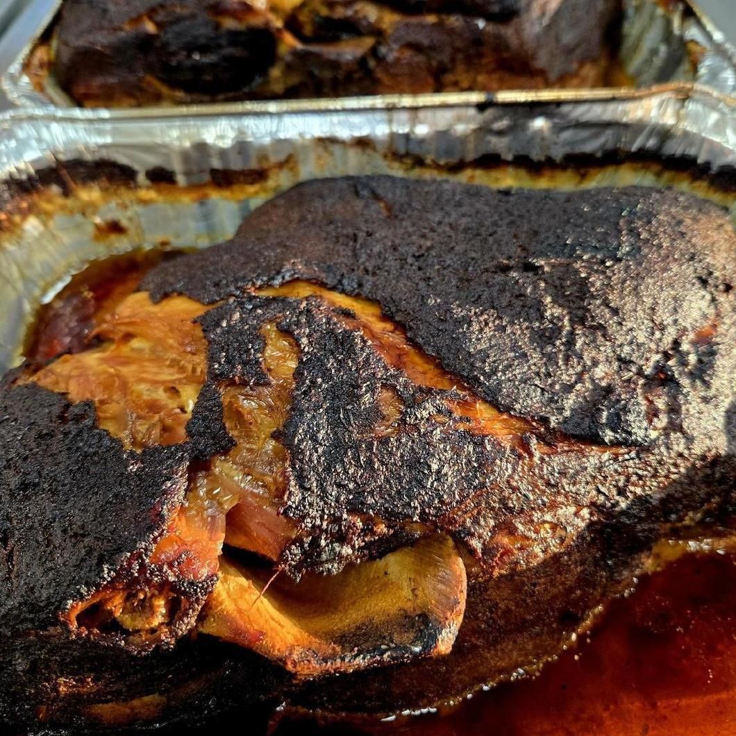 Charred roasted meat in a foil pan, with dark crust and orange juices visible