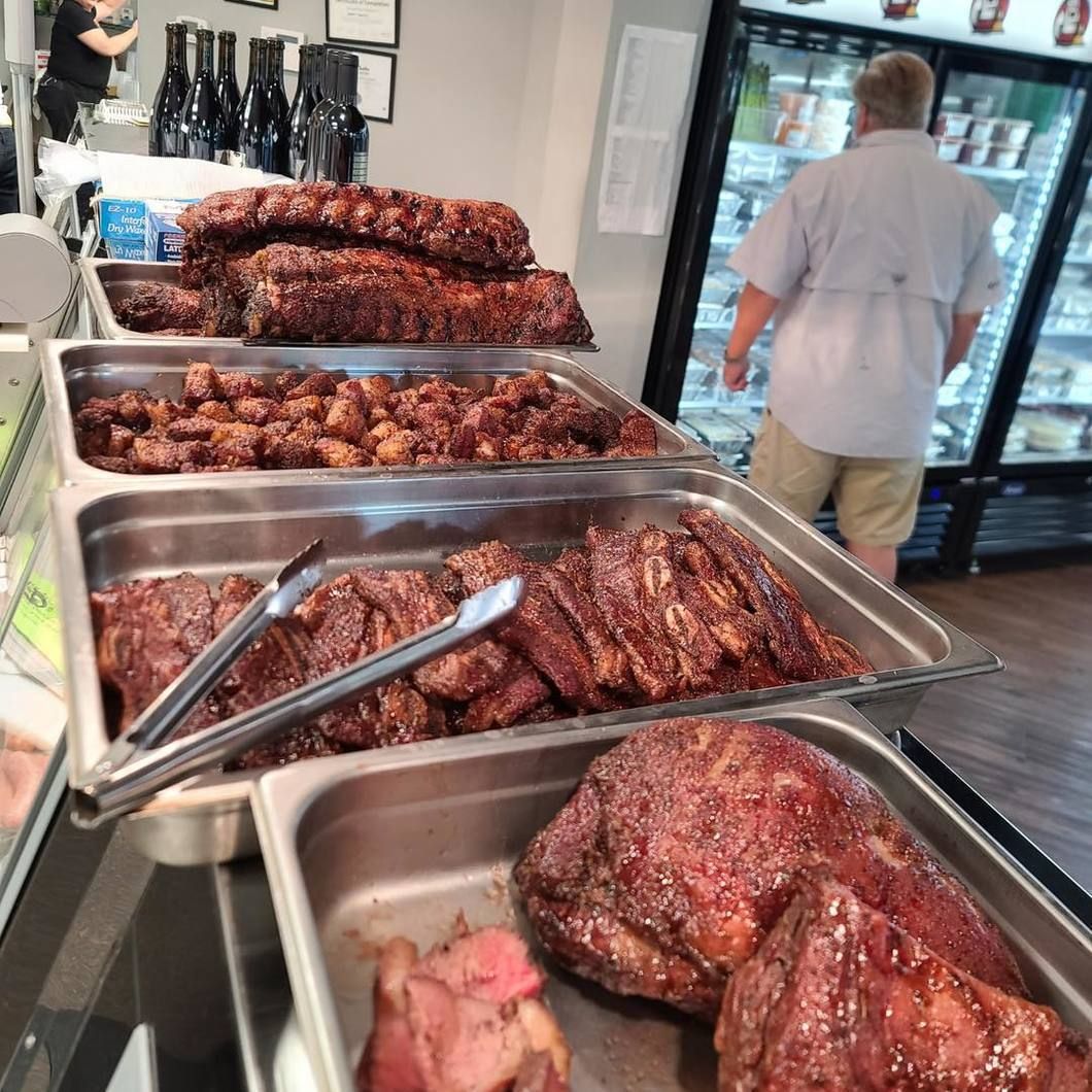 Trays of glazed smoked meat on a buffet counter, with a person standing by a glass refrigerator.