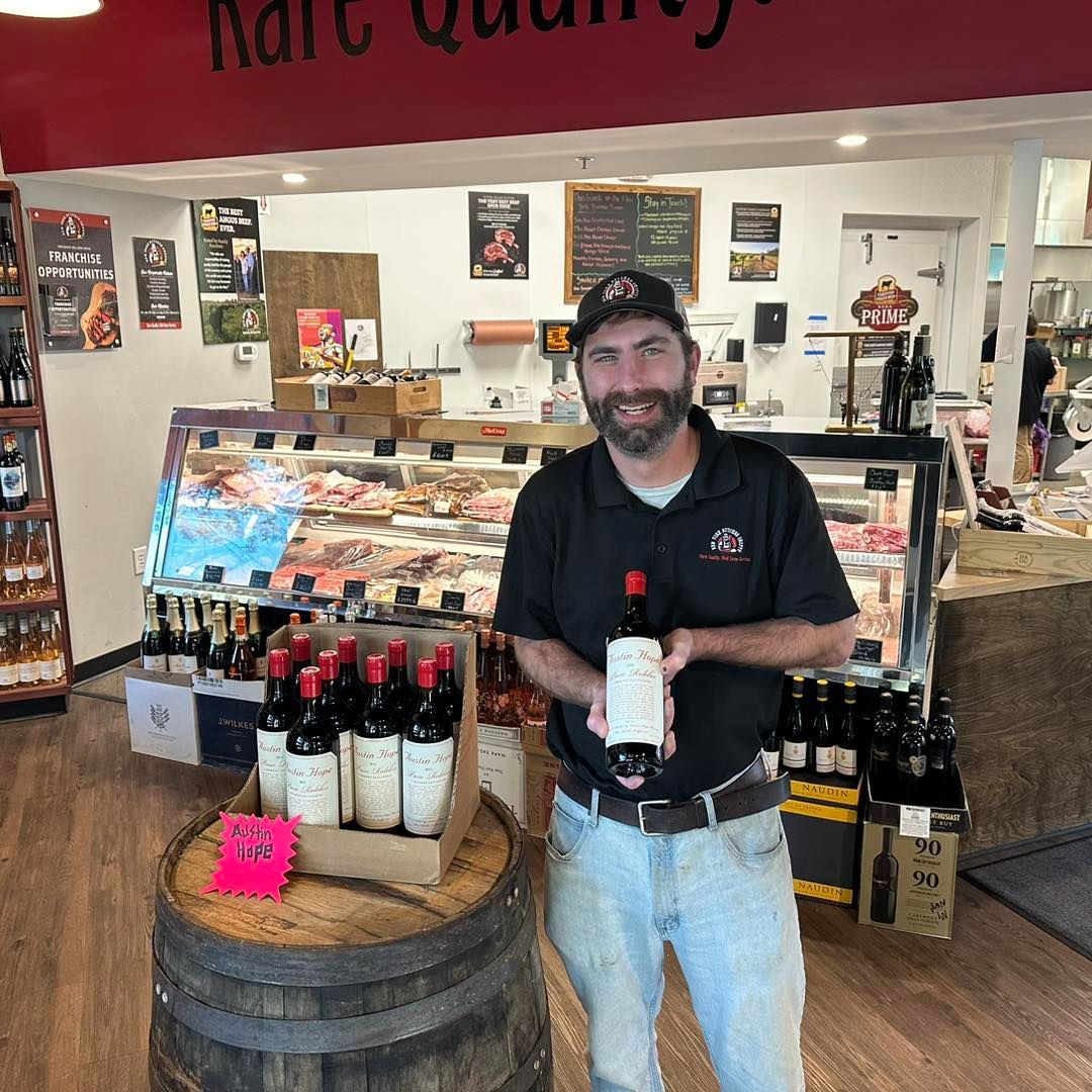 Man holding a wine bottle in a liquor store, standing by a display of bottled wine.