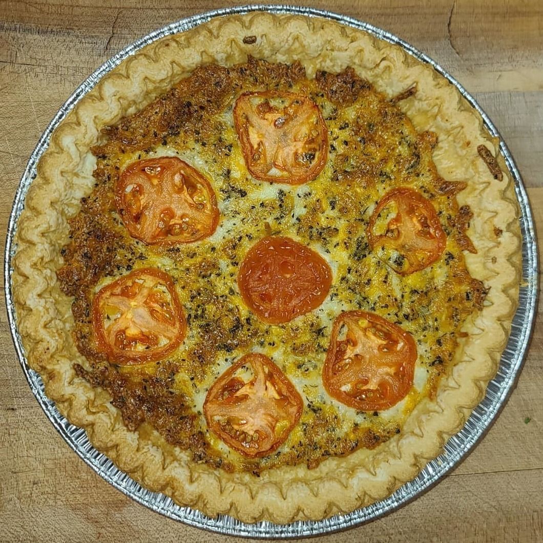 Cheese pizza with tomato slices in a foil pan on a wooden table