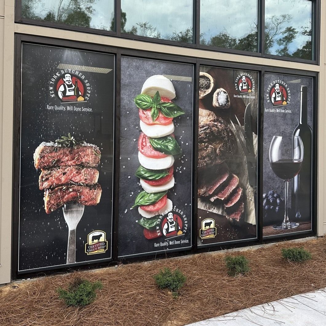 Storefront window decals advertising grilled steak, tomato-mozzarella skewers, and wine.