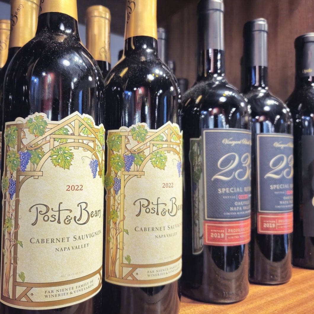 Assorted wine bottles on a shelf, including 2022 Post & Beam Cabernet Sauvignon and 23 Smuggler's wines.