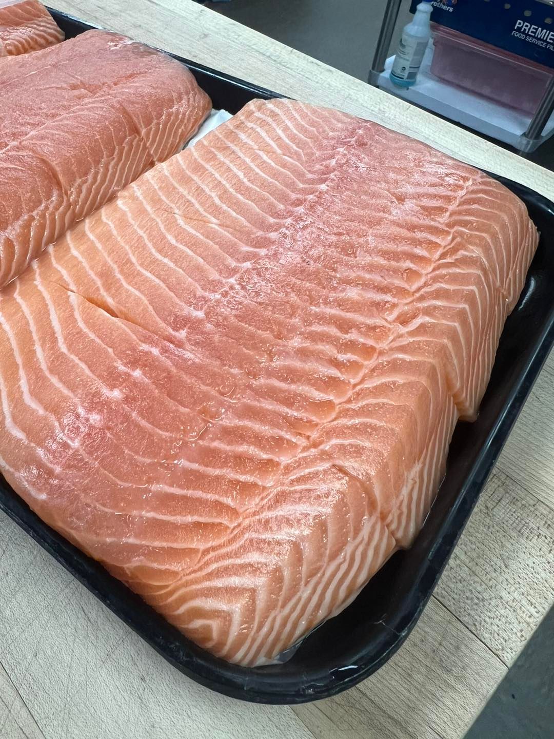 Raw salmon fillets in a black tray, showing pink and white textured flesh.