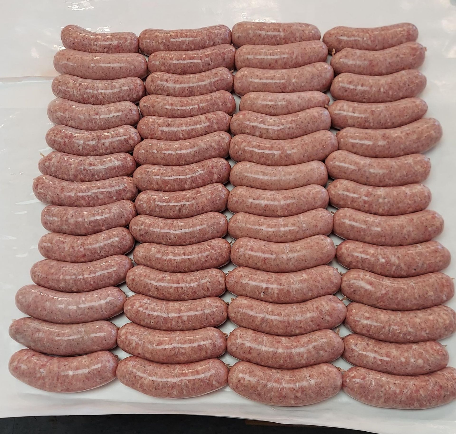 Rows of raw, pink sausages arranged closely on a white surface.