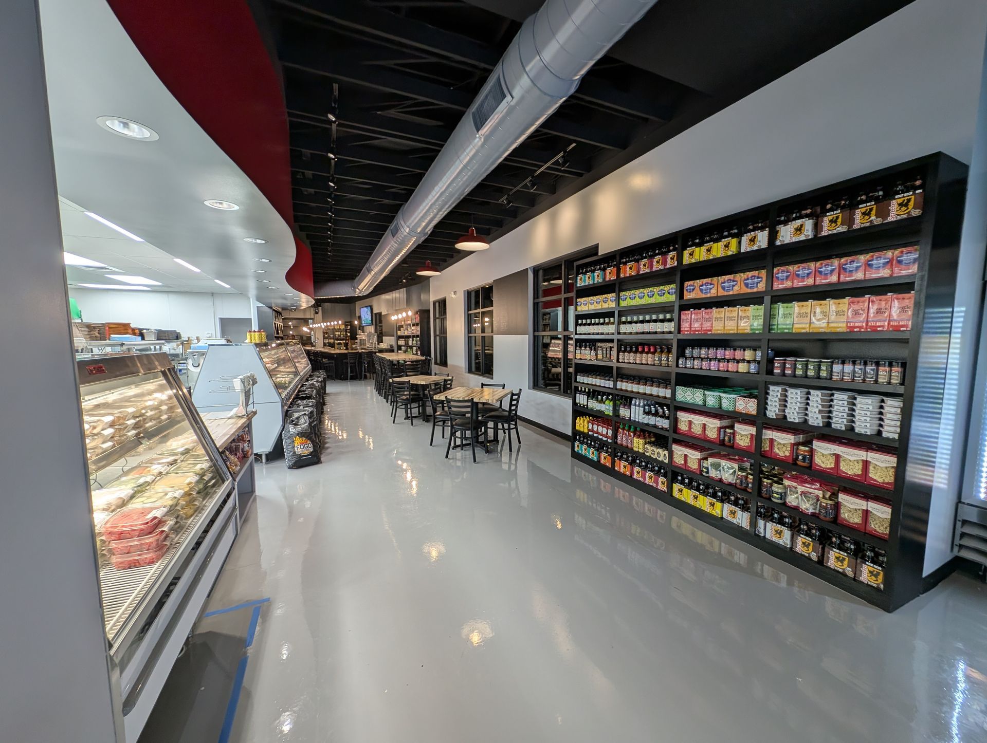 Bright modern convenience store aisle with shelves of snacks, drinks, and a few tables in the center.